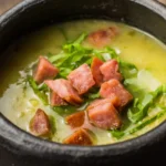 Caldo Verde tradicional com batatas, calabresa e couve manteiga, servido em uma tigela com croutons e azeite.