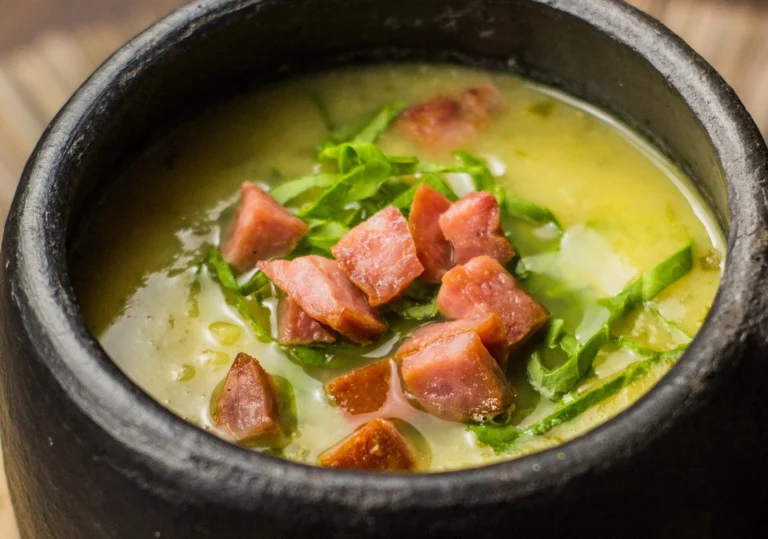 Caldo Verde tradicional com batatas, calabresa e couve manteiga, servido em uma tigela com croutons e azeite.