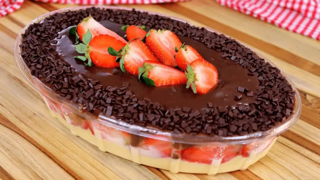 Imagem de uma sobremesa montada em camadas com morangos frescos, brigadeiro branco e ganache de chocolate ao leite em um refratário.