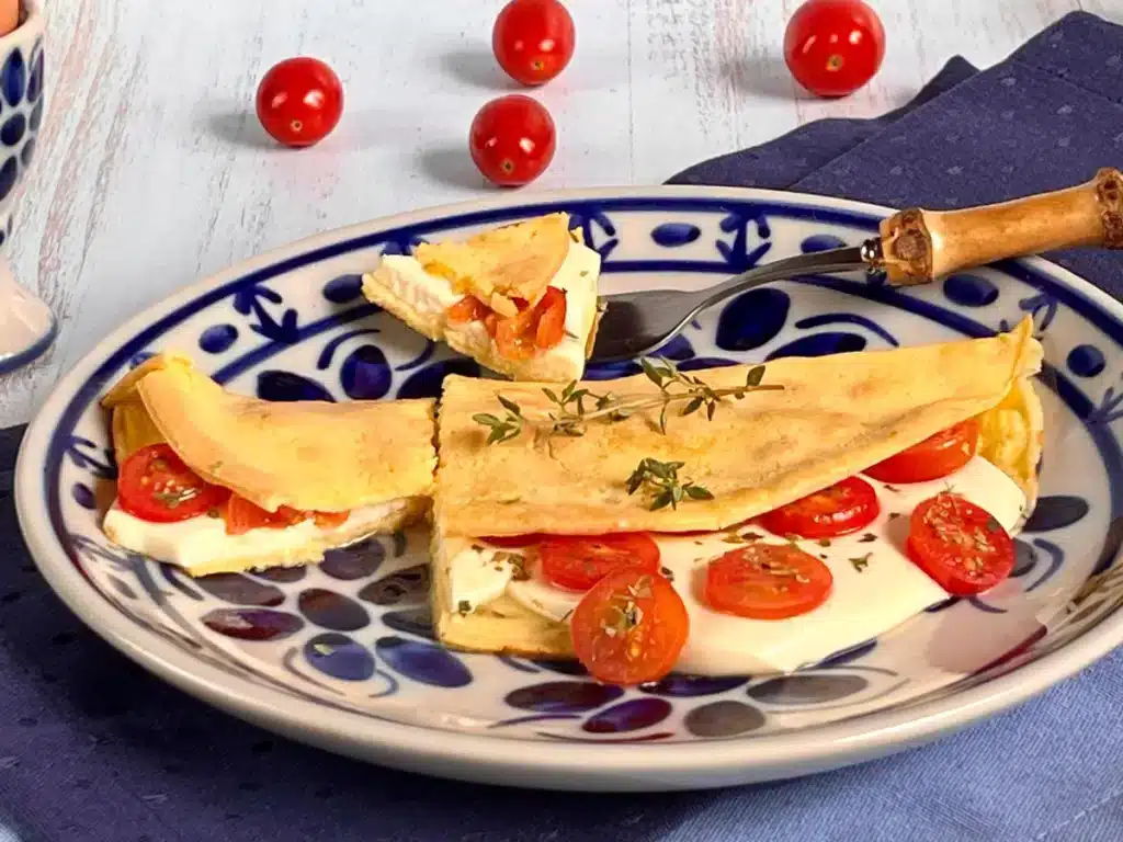 Crepioca dourada ao ponto, recheada com queijo fresco, tomates-cereja fatiados e orégano, servida em um prato branco, destacando seu visual apetitoso e saudável.