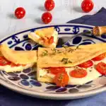 Crepioca dourada ao ponto, recheada com queijo fresco, tomates-cereja fatiados e orégano, servida em um prato branco, destacando seu visual apetitoso e saudável.
